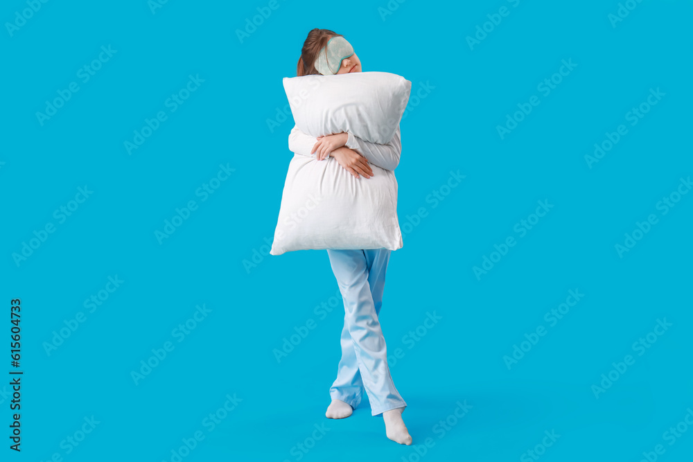 Cute little girl with sleep mask and pillow on blue background