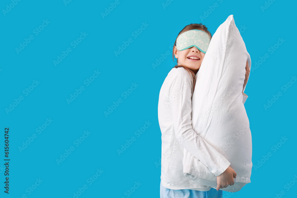 Cute little girl with sleep mask and pillow on blue background