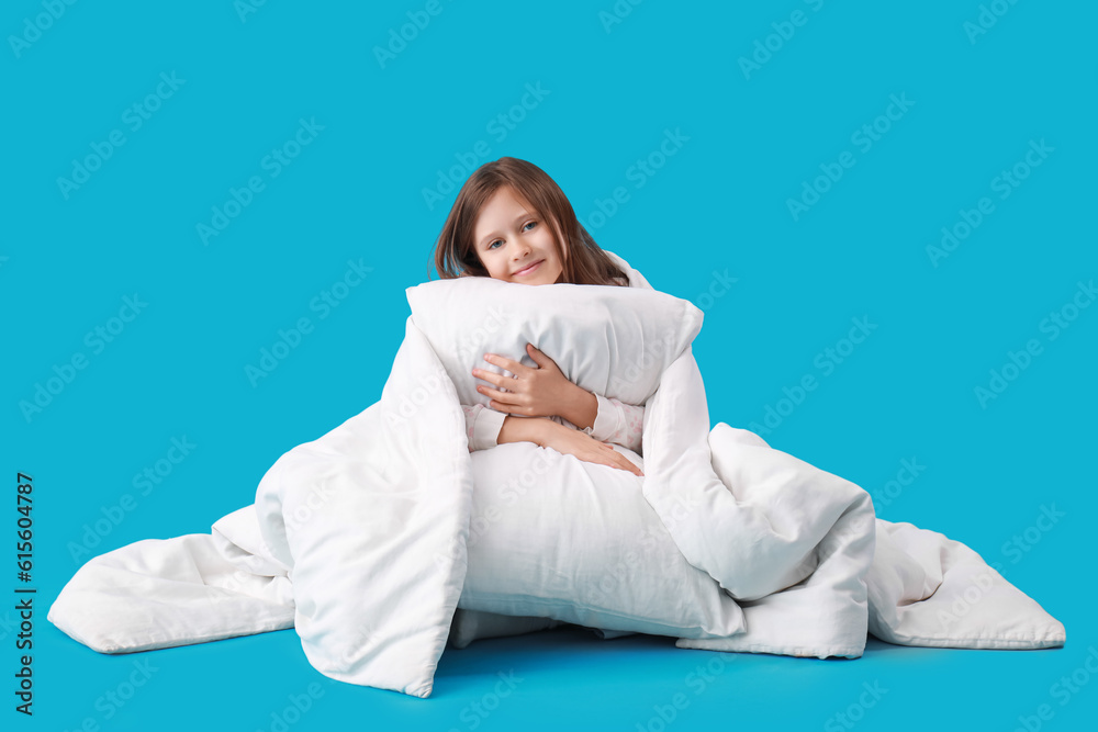 Little girl with soft pillow and blanket on blue background