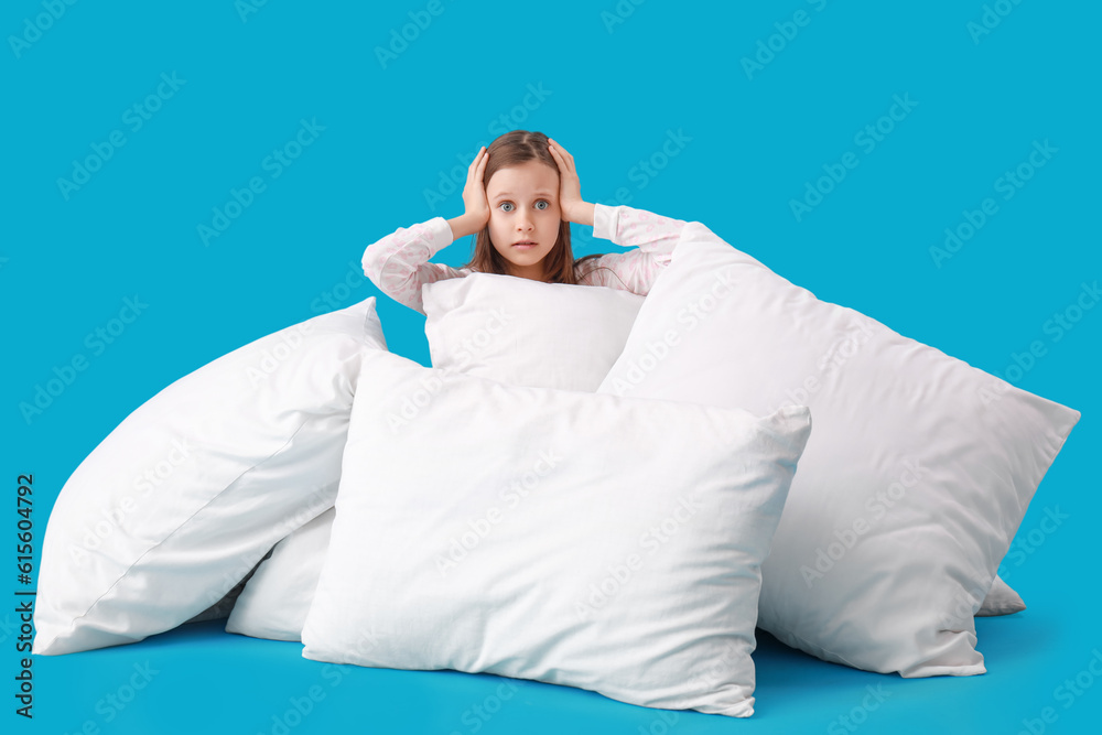 Shocked little girl with many pillows on blue background