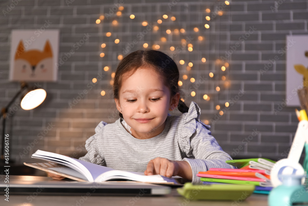 Little girl reading book at home late in evening