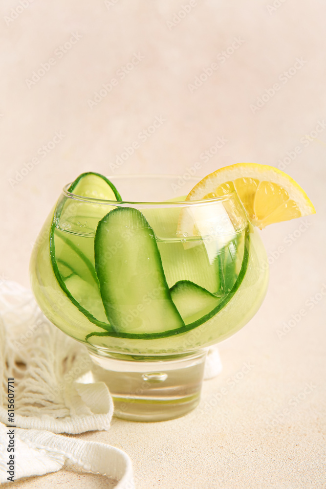 Glass of infused water with cucumber slices and string bag on beige background