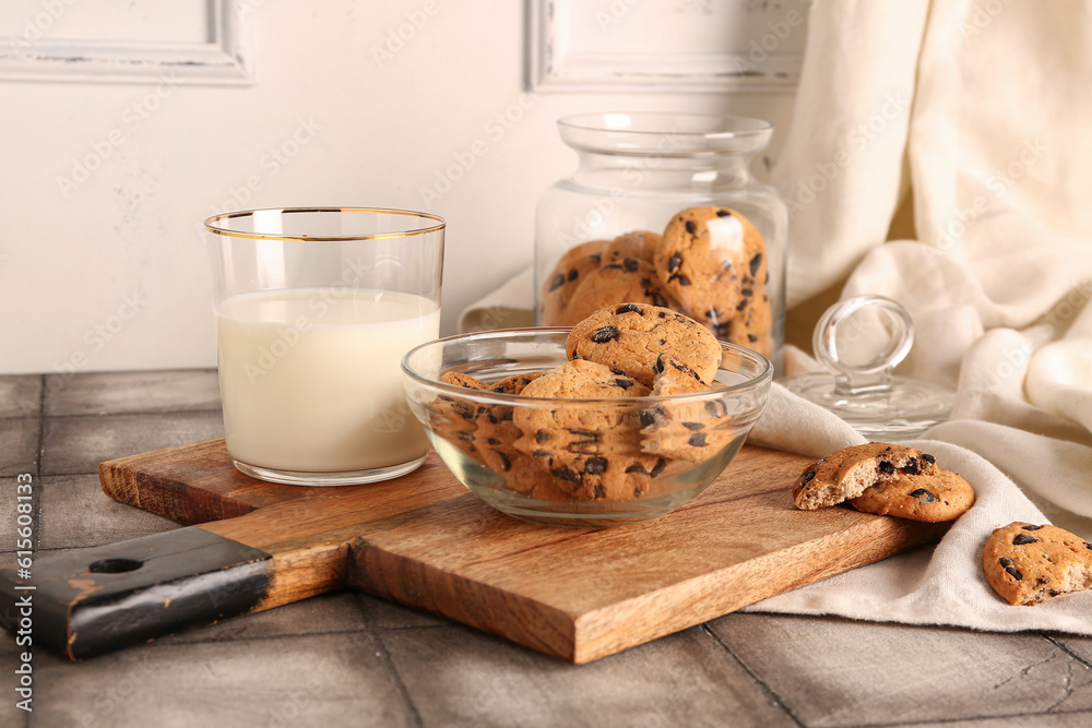 Wooden board with cookies, cup of milk and towel on grey tile table