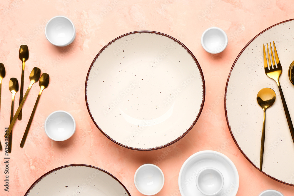 Clean plate, bowl and set of golden cutlery on pink table