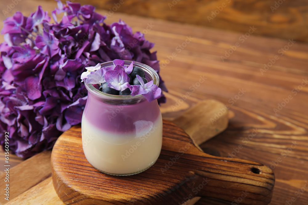 Glass of panna cotta with blueberry and beautiful hydrangea flowers on wooden background