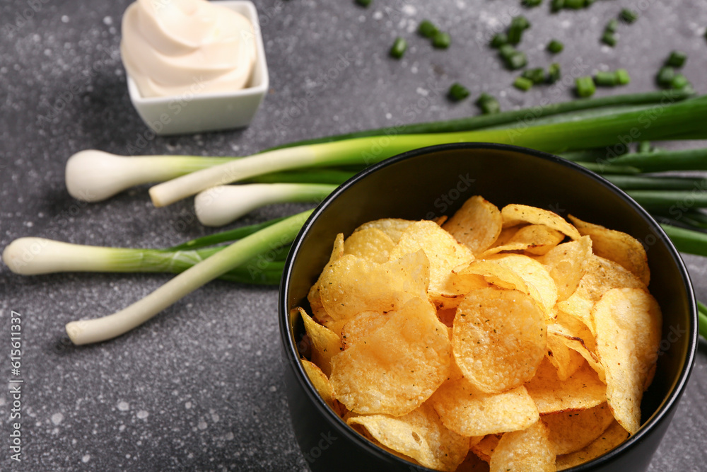 Bowl of tasty sour cream with sliced green onion and potato chips on grey background