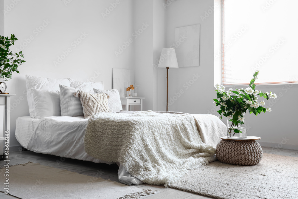 Interior of light bedroom decorated with blooming jasmine flowers in vase