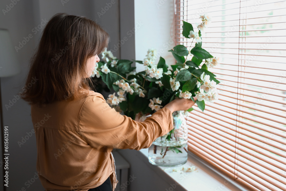 Woman enjoying blooming jasmine flowers in vase on windowsill