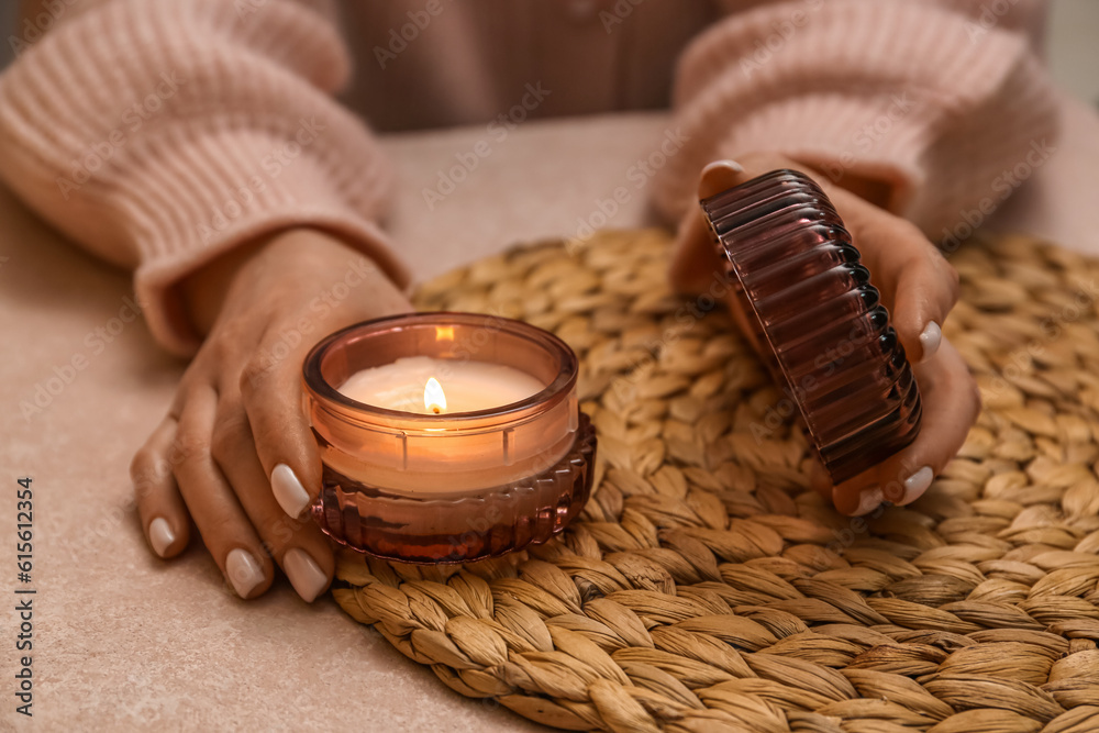 Woman holding holder with burning candle on table in evening, closeup