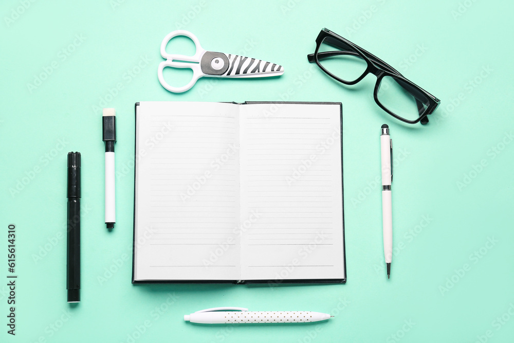 Open notebook with eyeglasses and different stationery on turquoise background