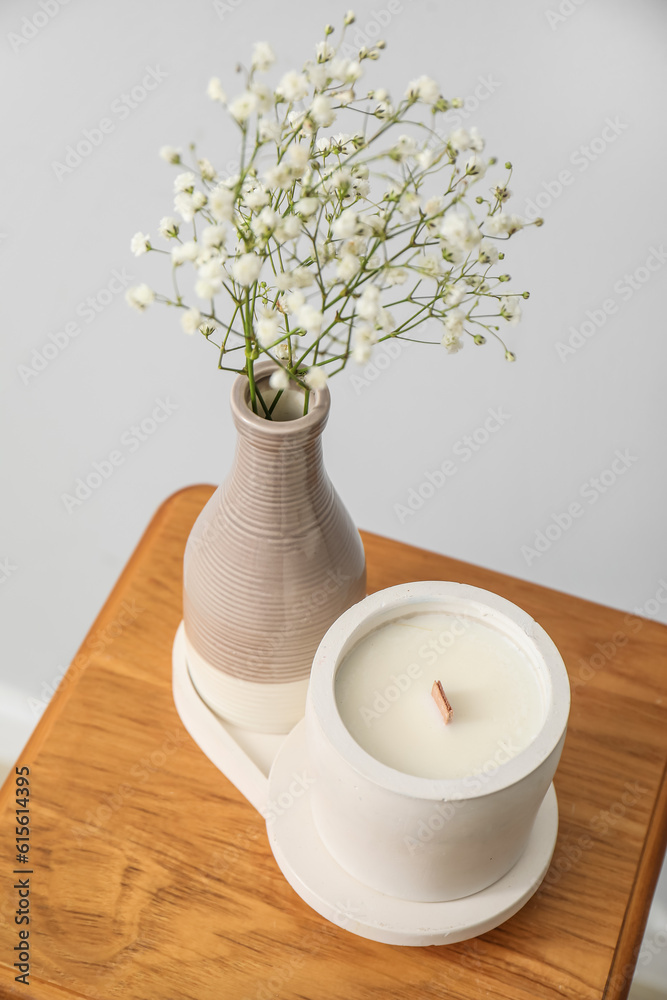 Gypsophila flowers and candle on chair near light wall in room, closeup