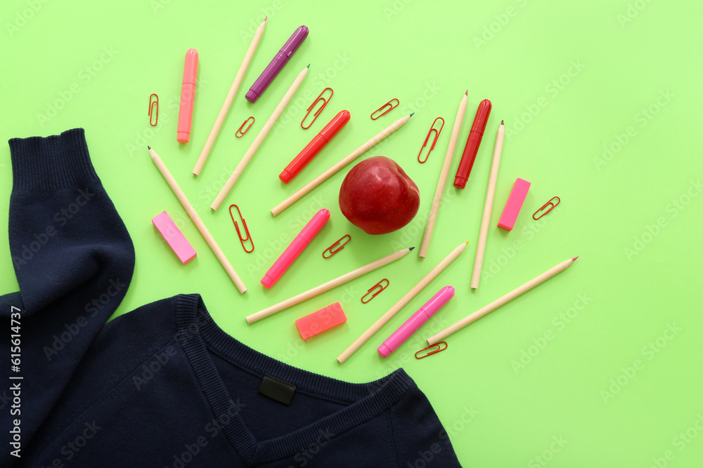 Stylish cardigan with fresh red apple and different stationery on green background