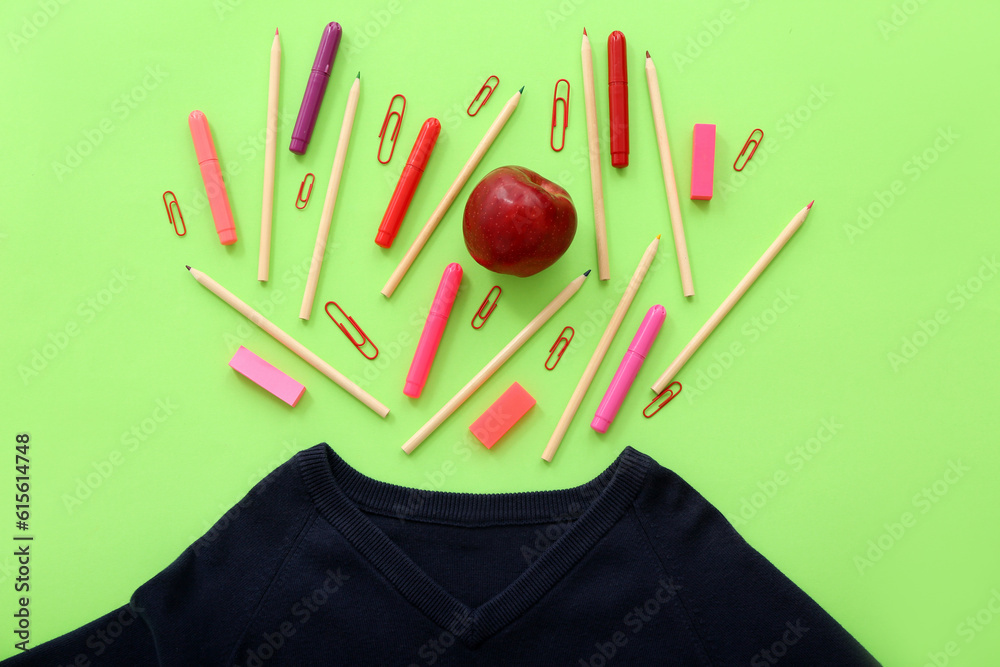 Stylish cardigan with fresh red apple and different stationery on green background