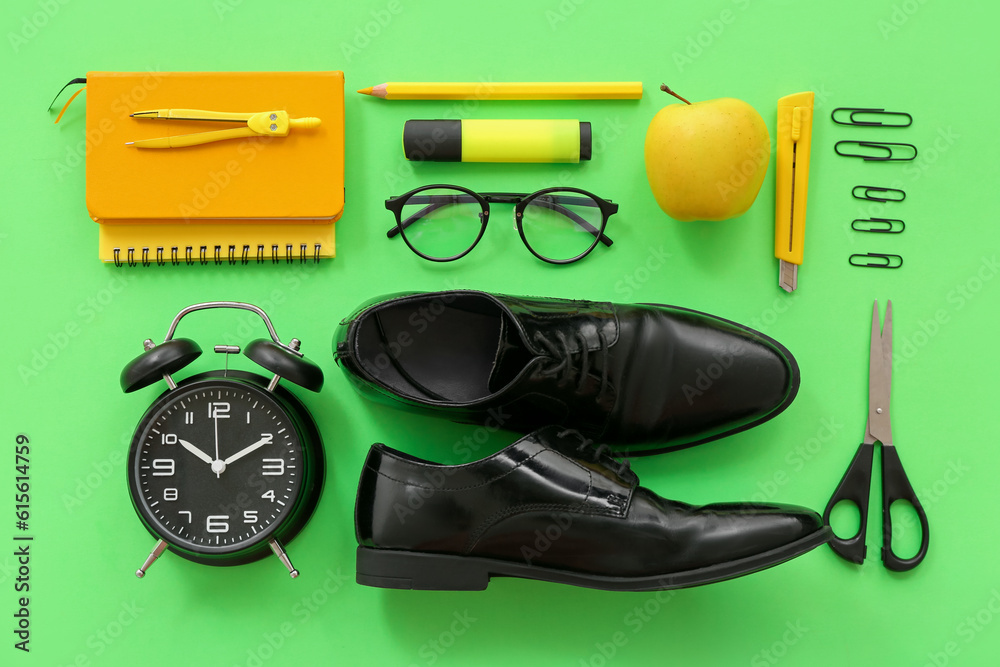 Classic shoes with fresh apple, eyeglasses and different stationery on green background