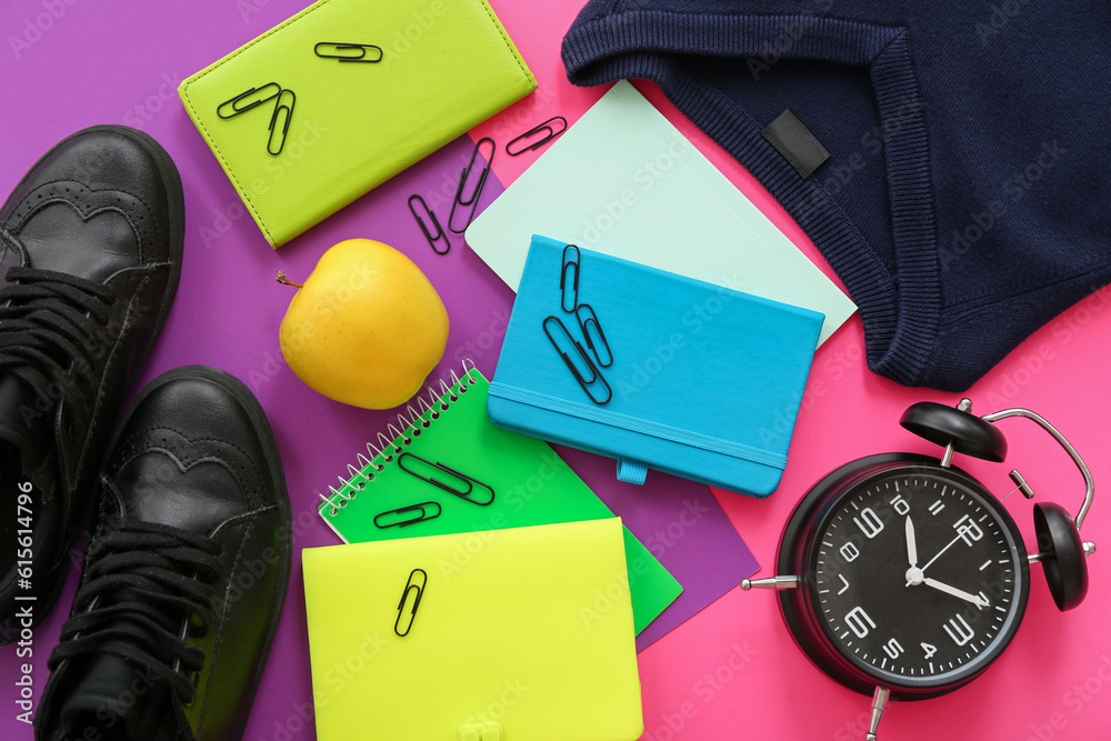 School uniform with fresh apple, alarm clock and different stationery on color background