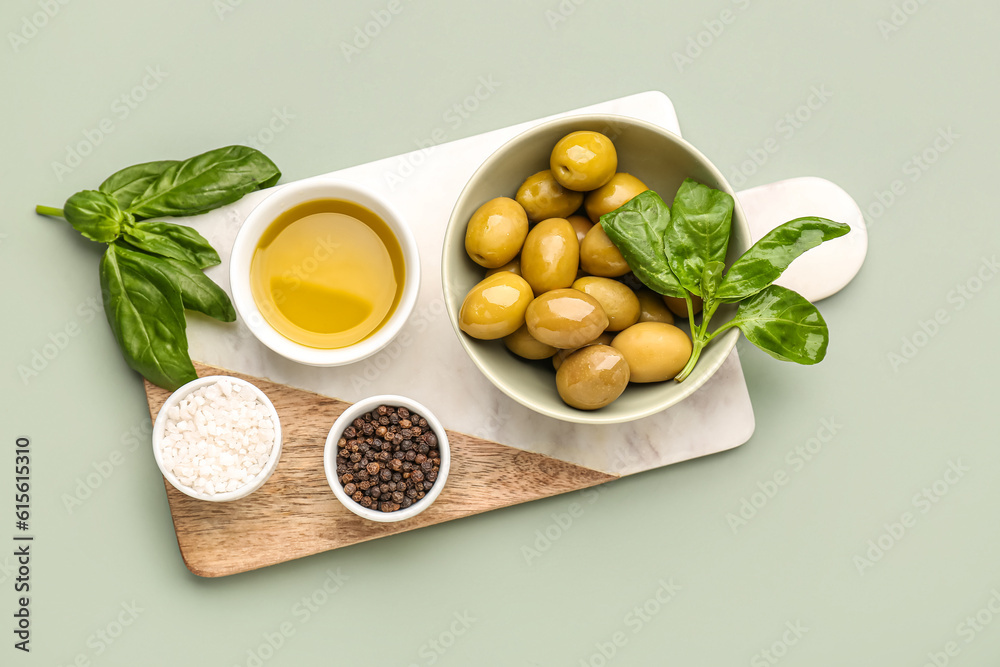 Bowls with ripe olives and oil on green background