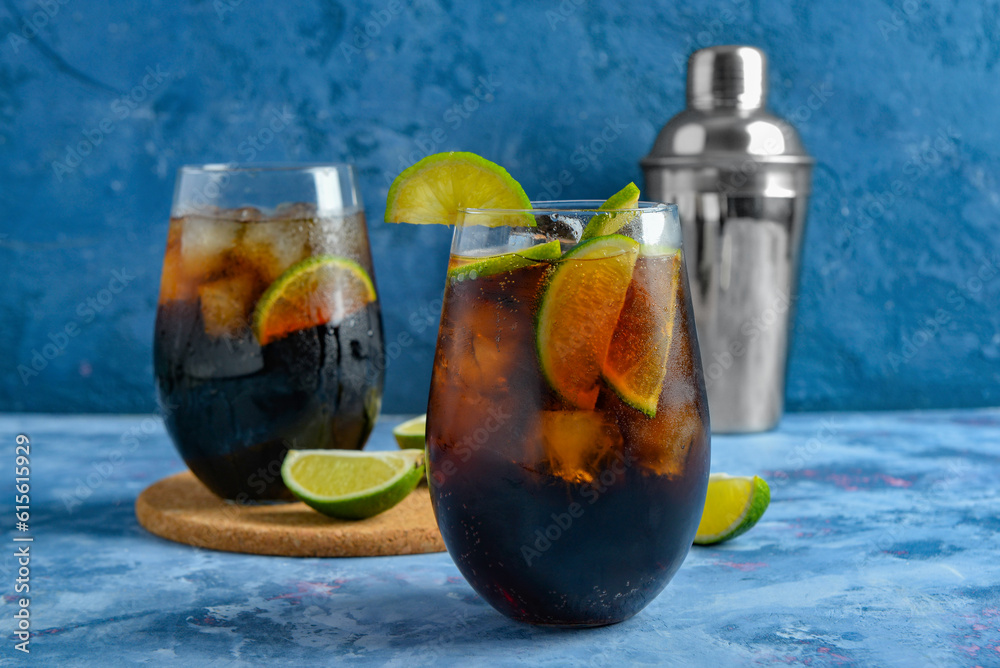 Glasses of cold Cuba Libre cocktail and shaker on blue background