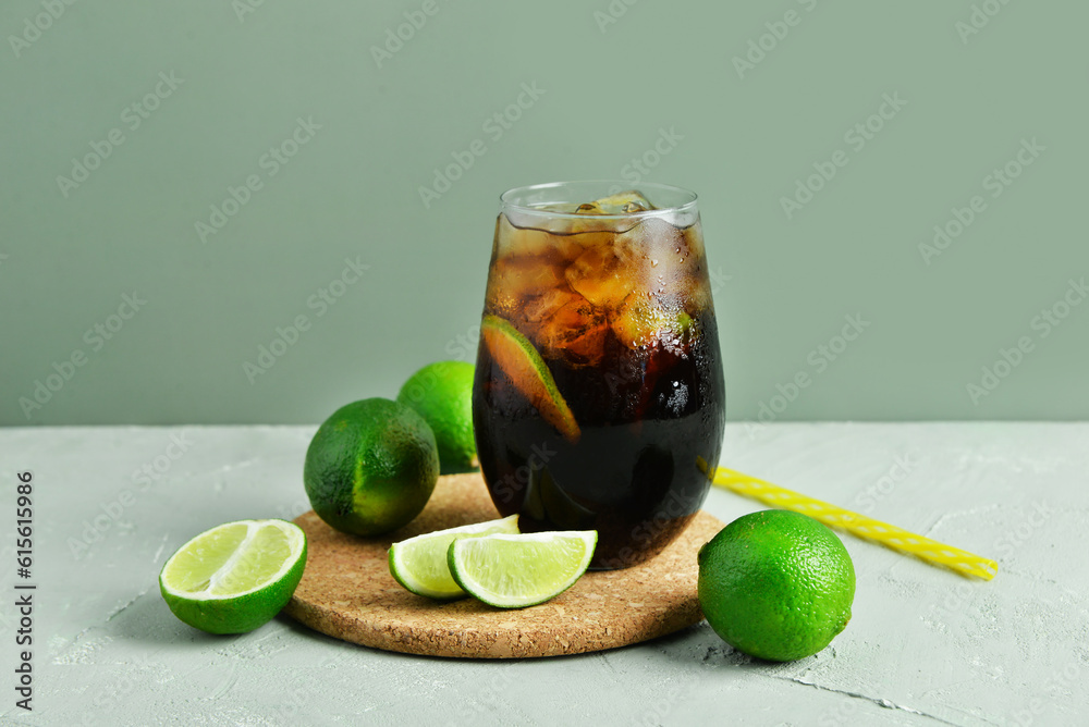 Glass of cold Cuba Libre cocktail and limes on grey background