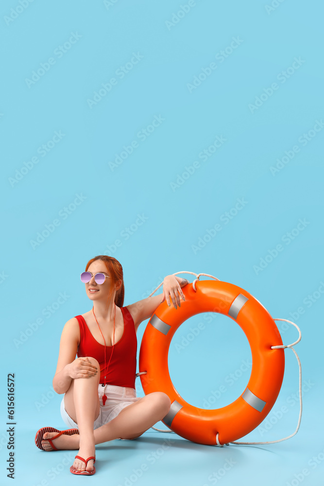 Female lifeguard with ring buoy sitting on blue background