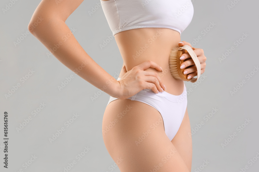 Young woman massaging her belly with anti-cellulite brush on light background, closeup