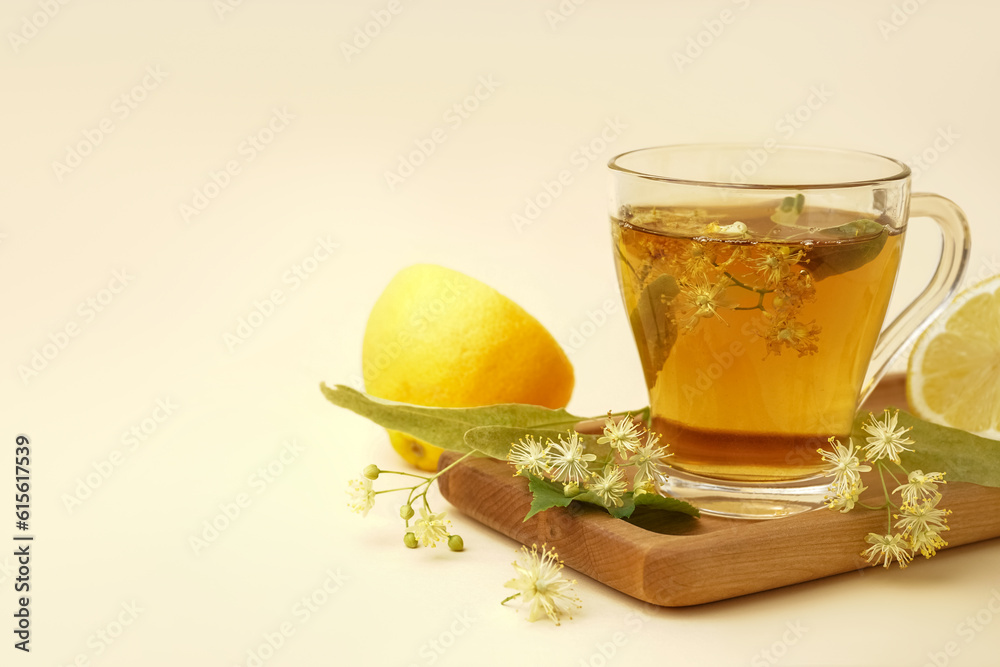 Board with glass cup of linden tea and lemon on beige background