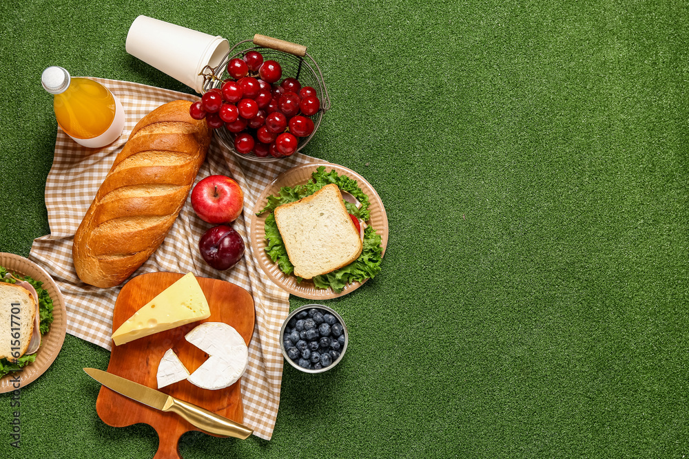 Composition with tasty food, juice and sandwiches for picnic on green background