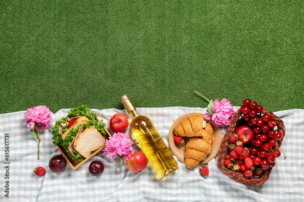 Composition with tasty food for picnic, wine and peony flowers on green background