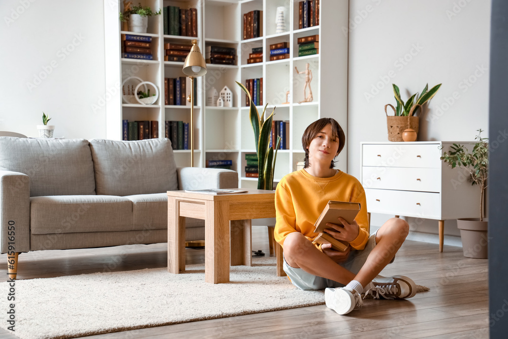 Teenage boy with books sitting on floor at home