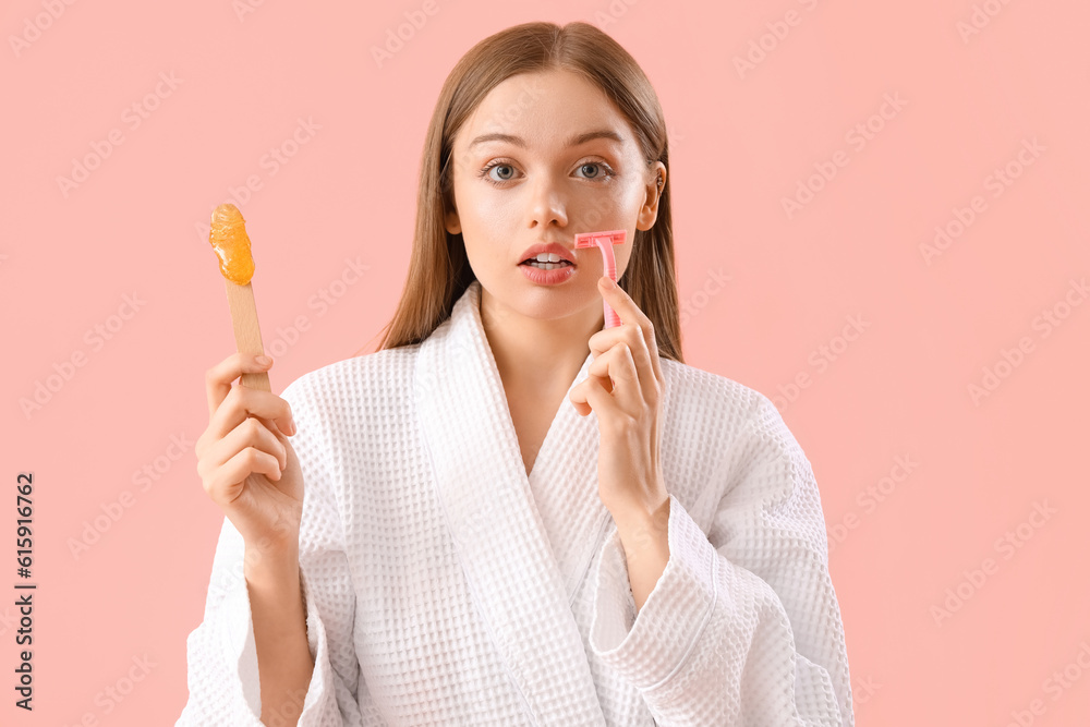 Young woman holding spatula with sugaring paste and razor on pink background