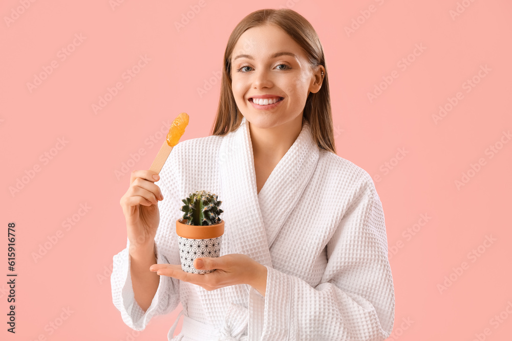 Young woman holding spatula with sugaring paste and cactus on pink background