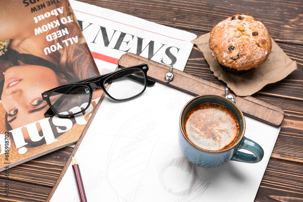 Cup of coffee with sketch, eyeglasses, muffin, magazine and newspaper on wooden background