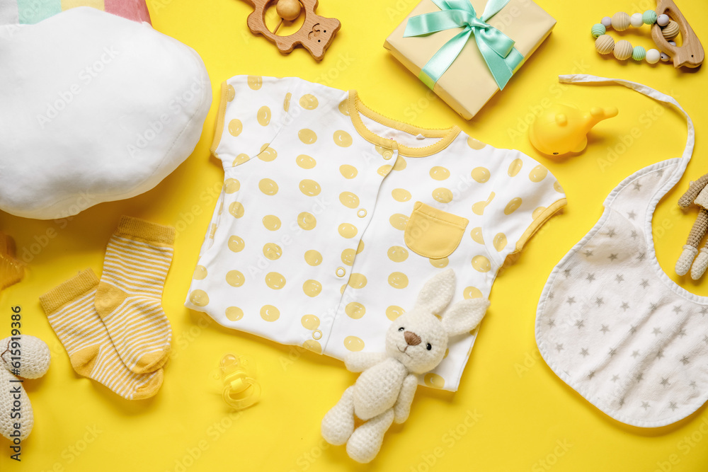 Composition with baby clothes and toys on yellow background