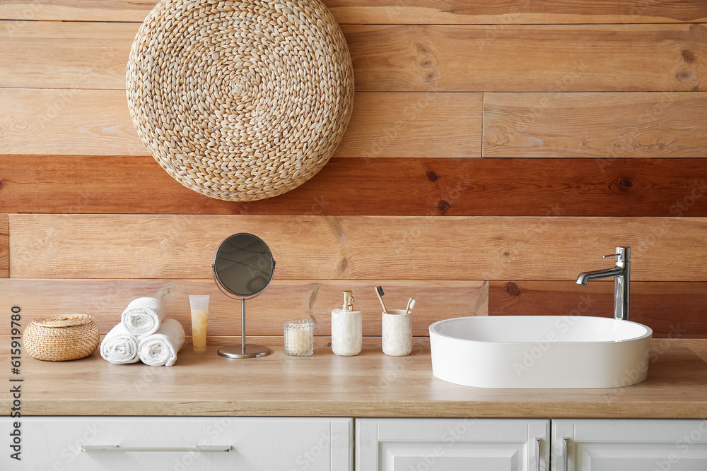 White sink with bath accessories on table near wooden wall