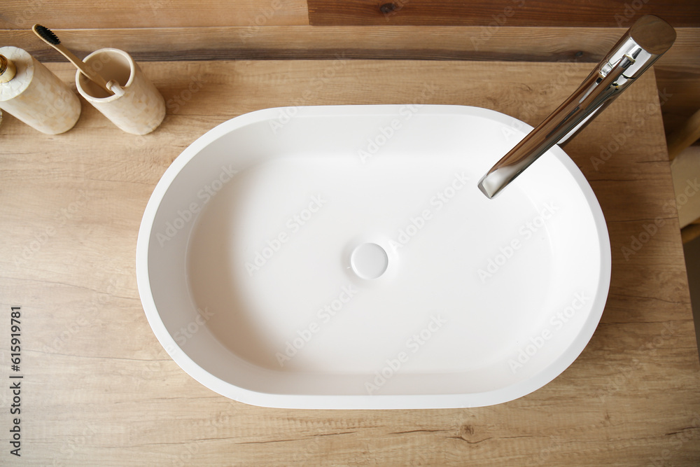 White sink with bath accessories on table near wooden wall