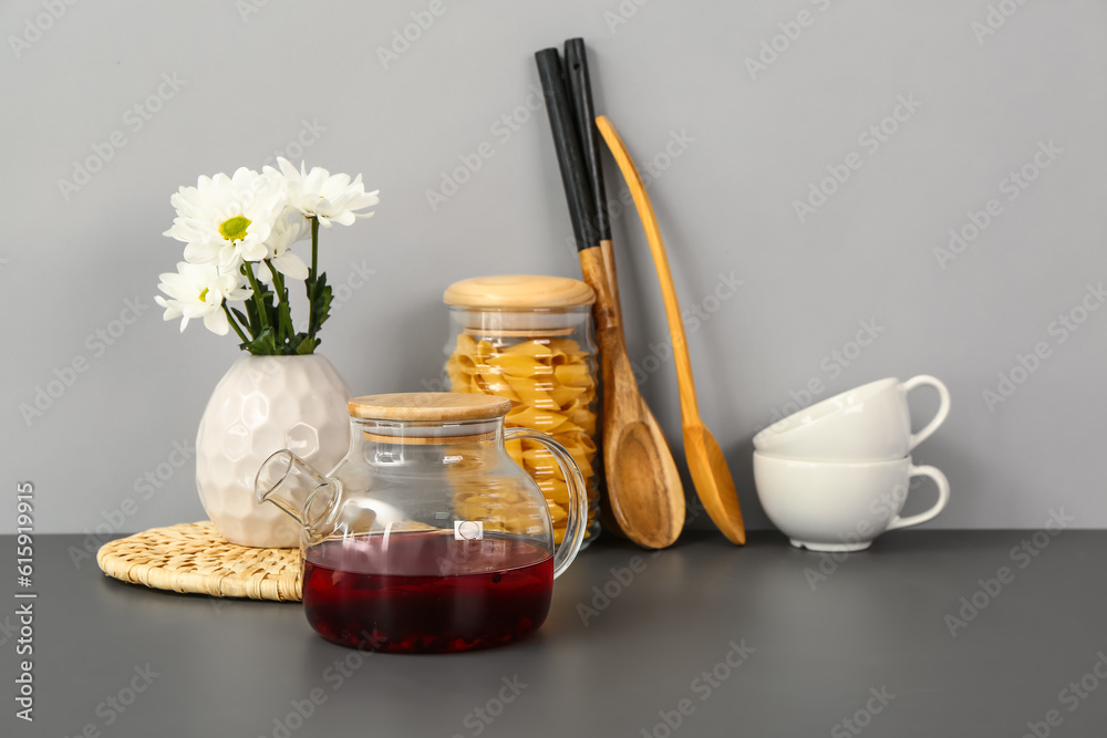 Teapot with flowers and different kitchen stuff on black table