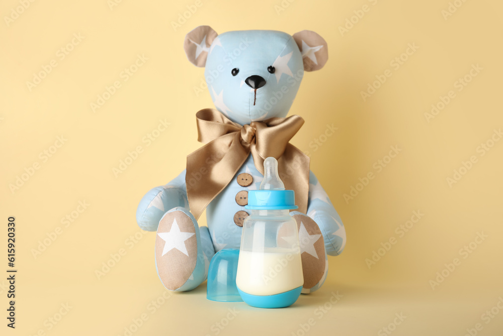 Teddy bear with bottle of milk for baby on pale yellow background