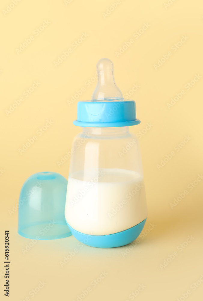 Bottle with milk for baby on pale yellow background