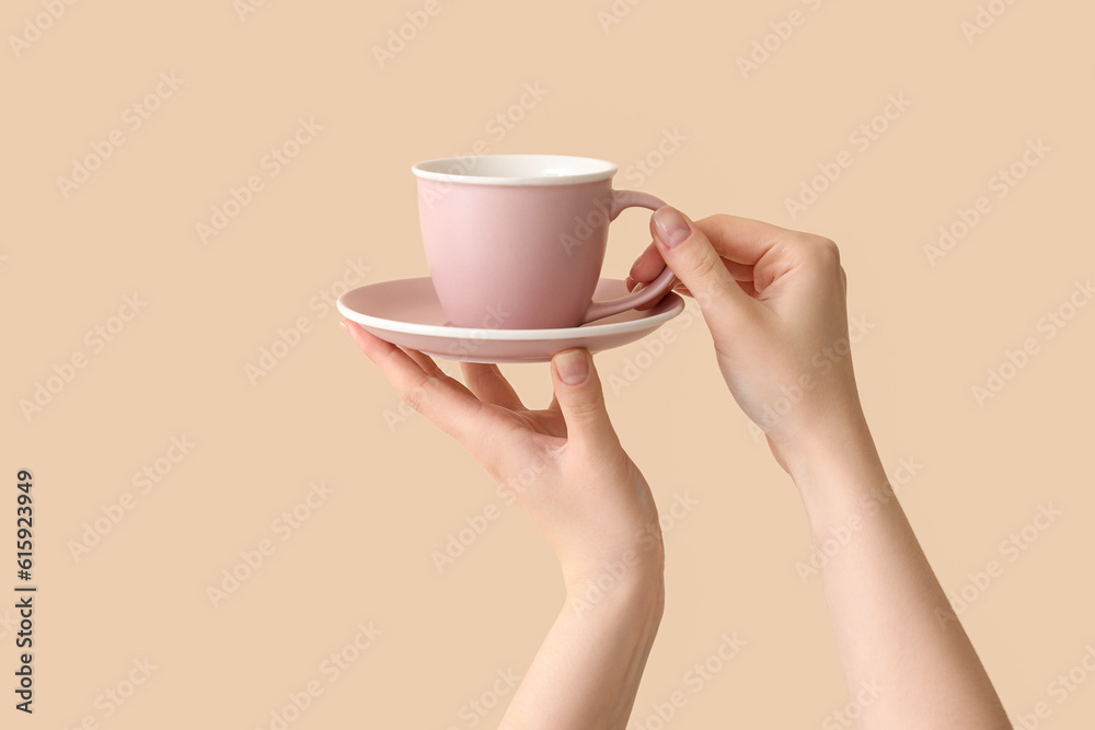 Female hands holding cup and saucer on beige background