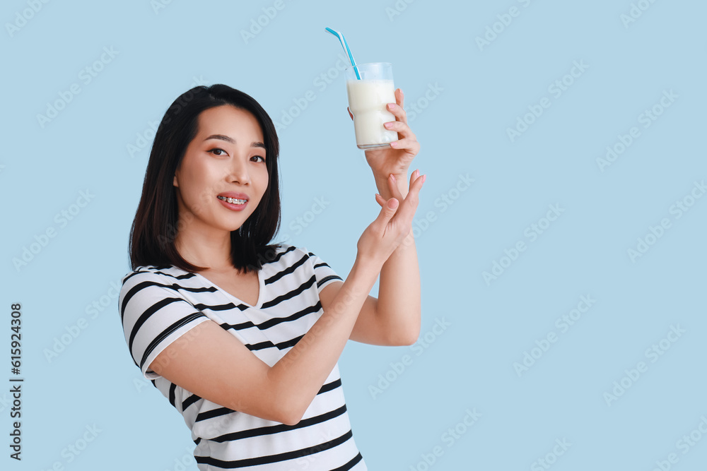 Beautiful Asian woman with glass of milk on light blue background