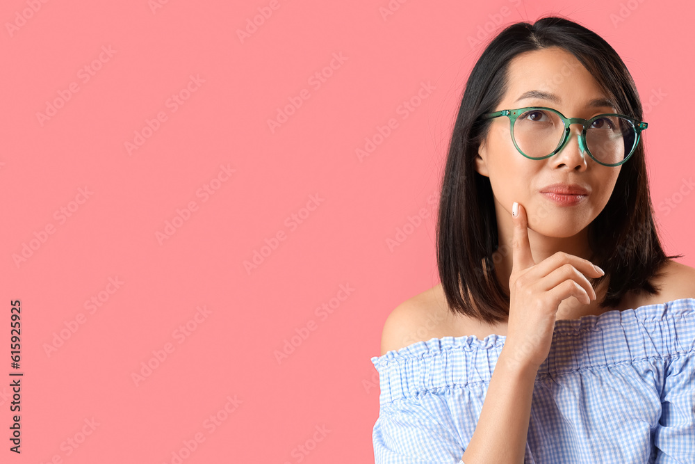 Thoughtful Asian woman in stylish eyeglasses on pink background, closeup