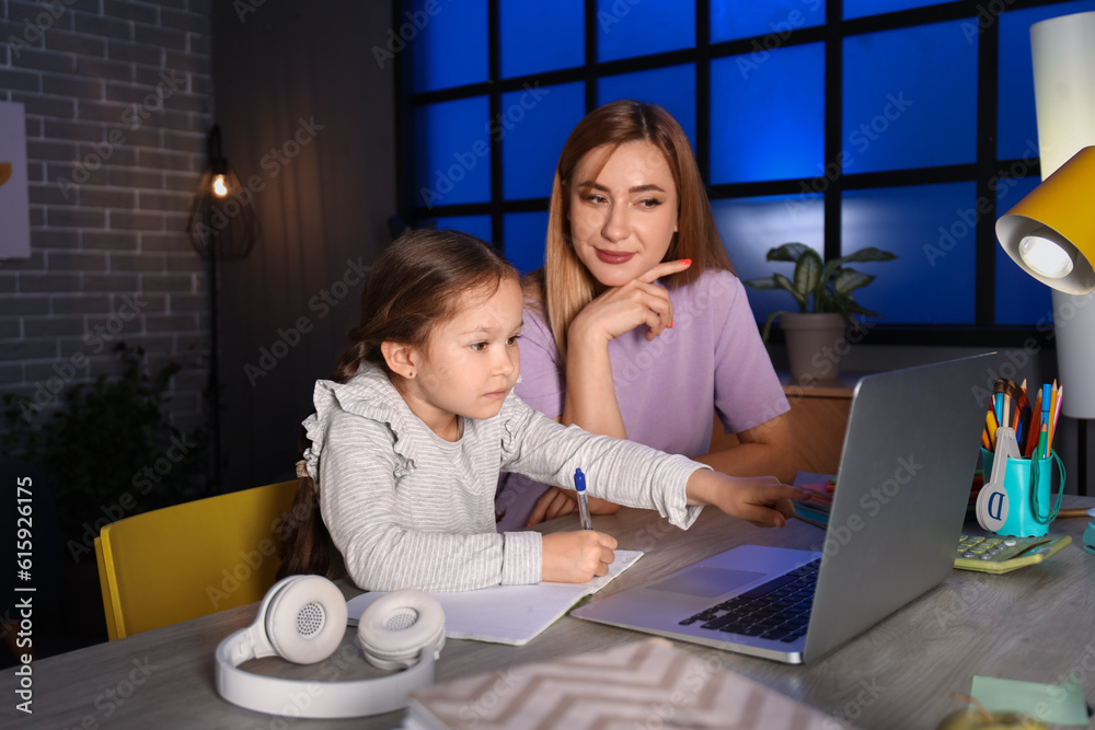 Little girl with her mother doing lessons at home late in evening