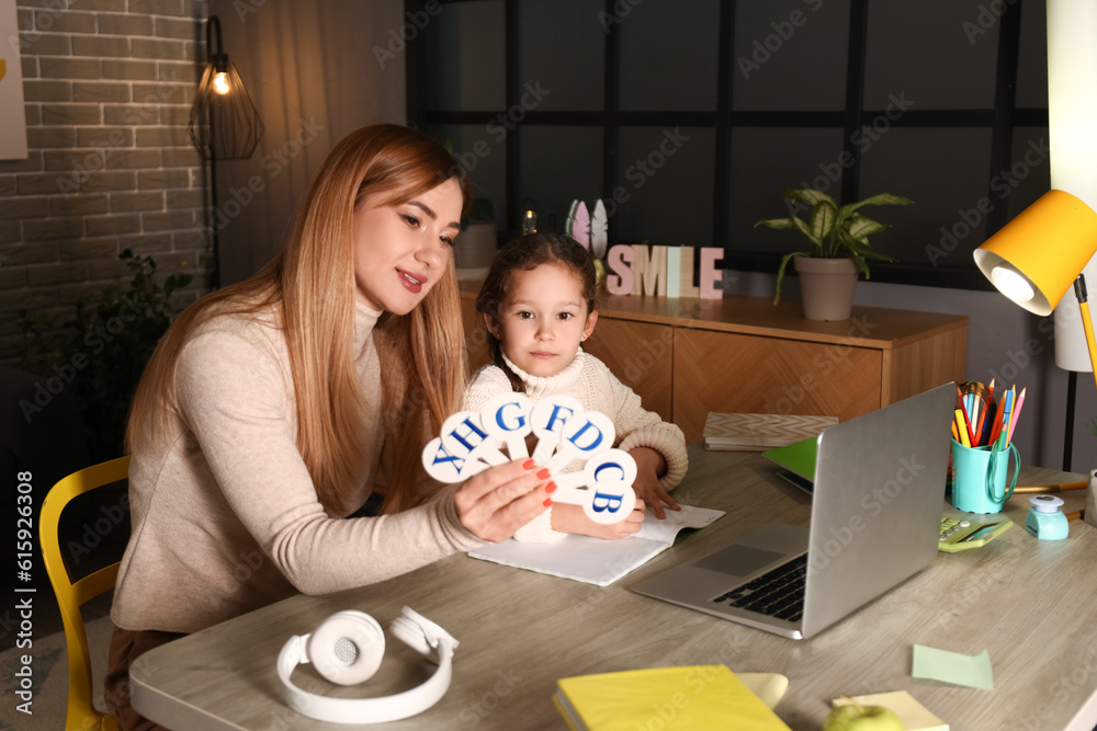 Little girl with her mother doing lessons at home late in evening