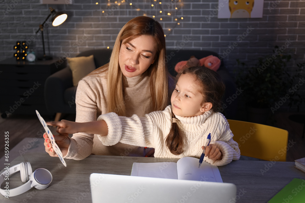 Little girl with her mother doing lessons at home late in evening