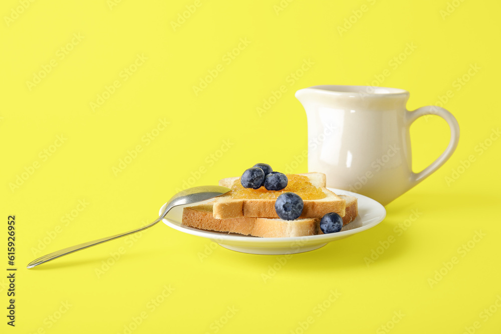 Plate of tasty toasts with peach jam, blueberry and milk in pitcher on yellow background