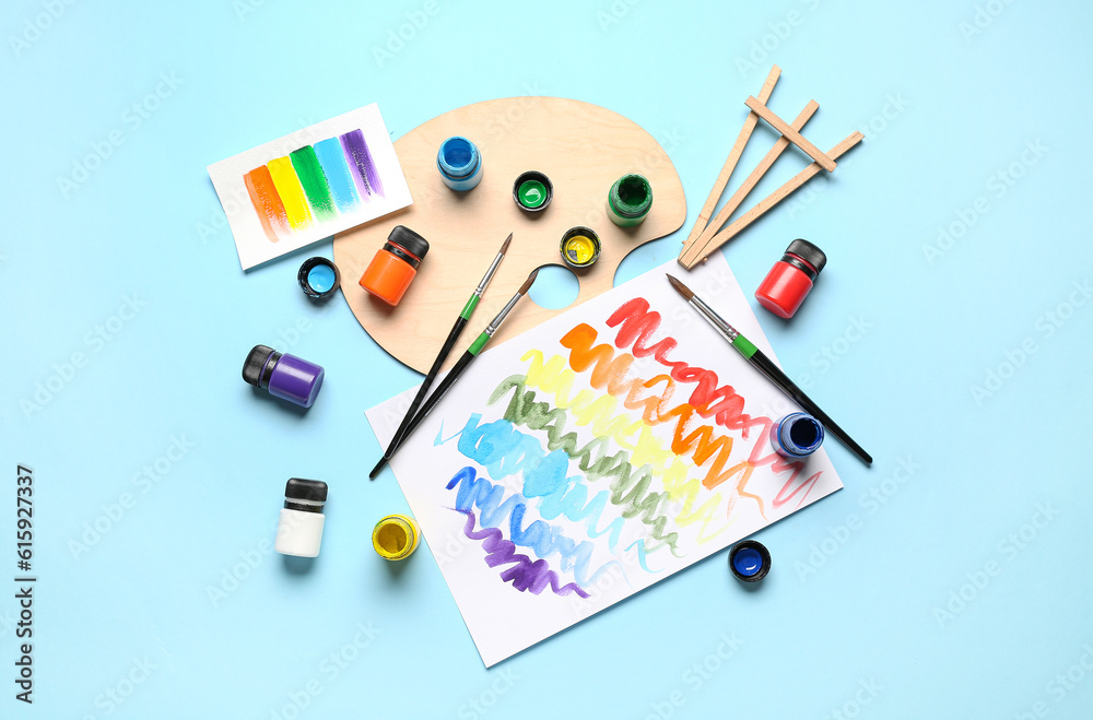 Composition with different paints, brushes and rainbow color palette on blue background