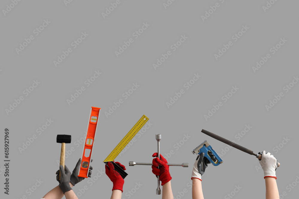 Female and male hands in gloves holding different construction tools on grey background