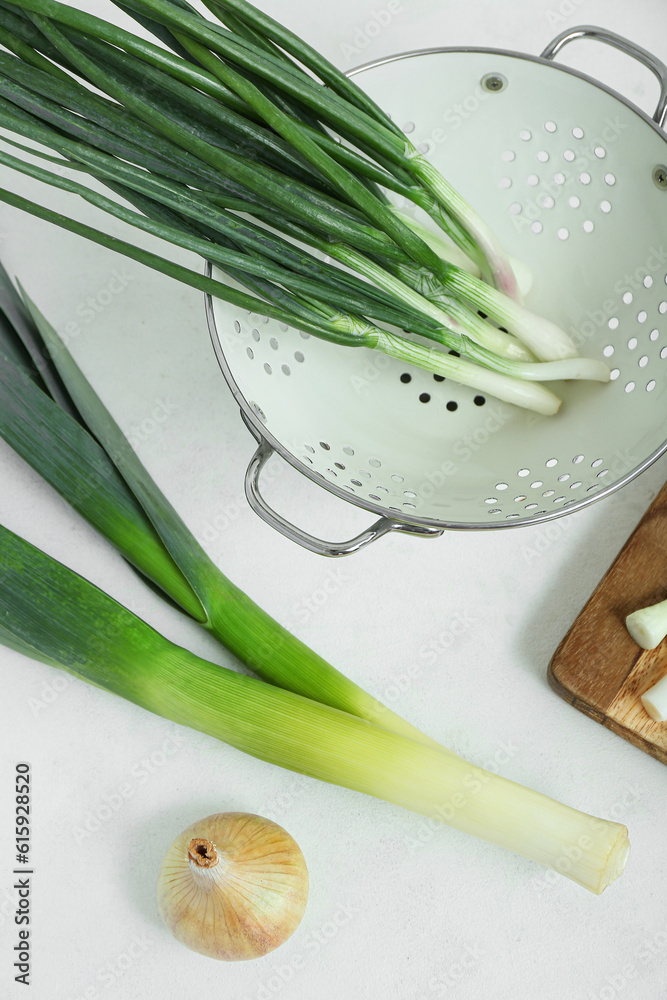 Colander with green onion and leeks on light background