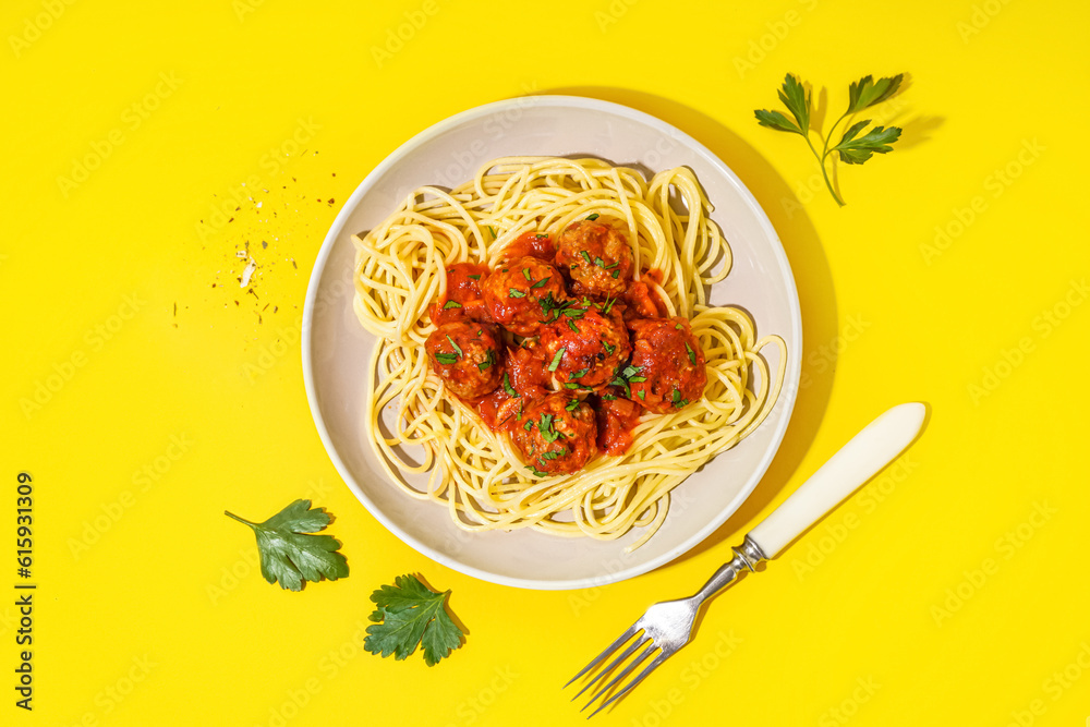 Plate of boiled pasta with tomato sauce and meat balls on yellow background