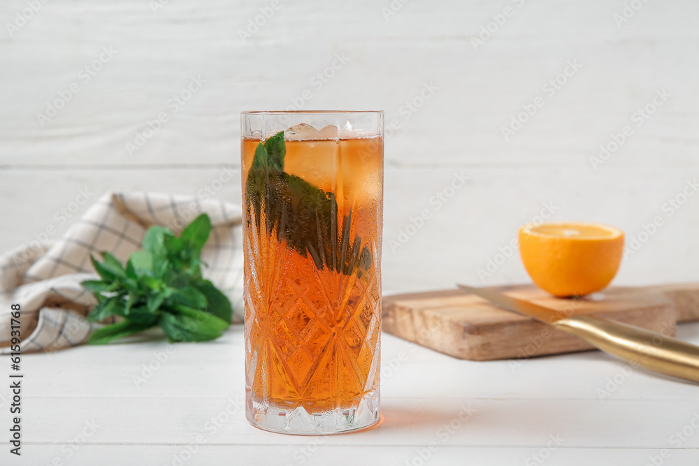 Glass of ice tea and board with orange on white wooden background