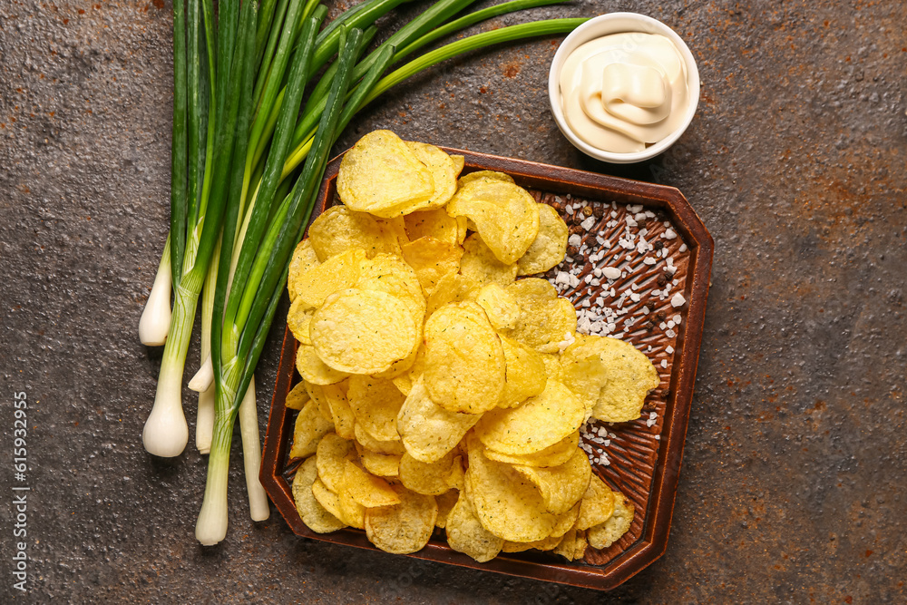 Bowl of tasty sour cream with green onion and potato chips on dark background